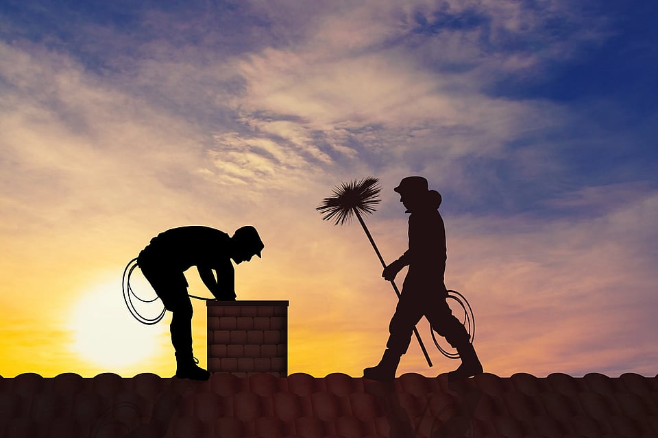 Two chimney sweeps silhouetted on a roof at dusk