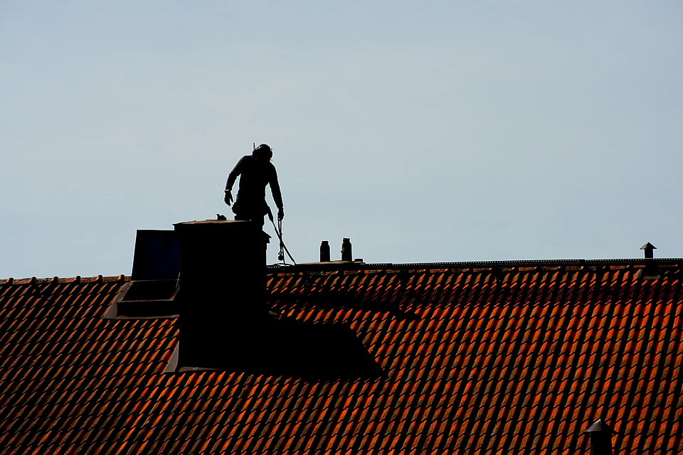 Adobe stock image of a silhoutted chimney sweep on a roof.