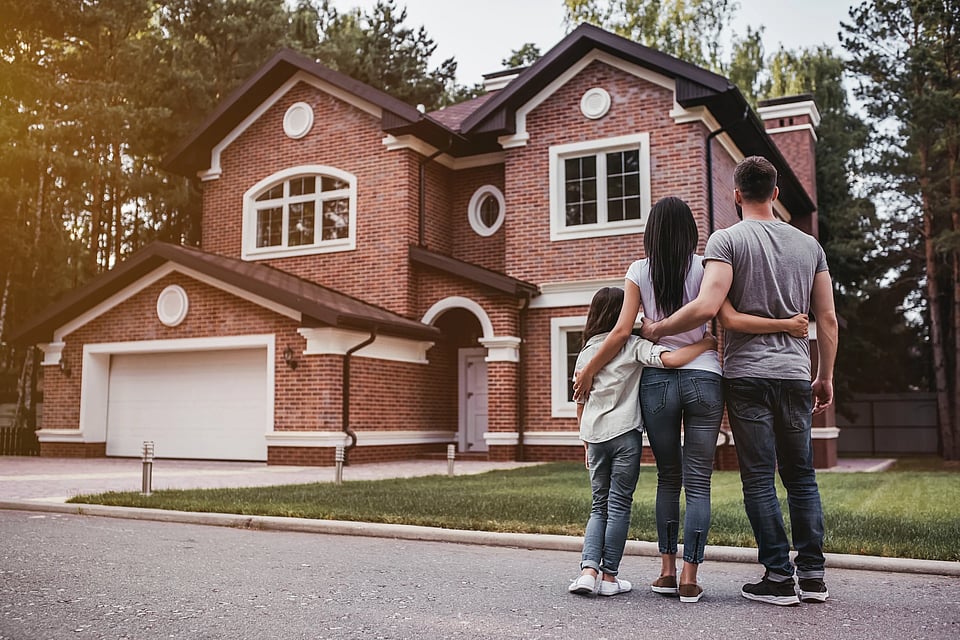 Adobe Stock image of a family standing outside of their home with their arms around each other.