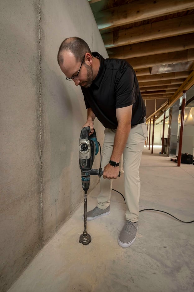 A technician drilling a hole for a new radon mitigation system.