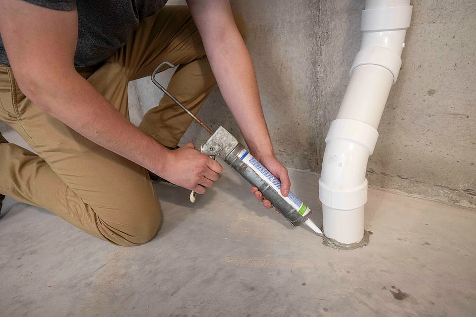 Image of a technician caulking the area where the radon mitigation system goes into the ground.