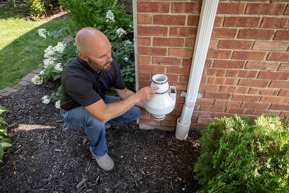A technician installing a new radon fan on the outside of a home.