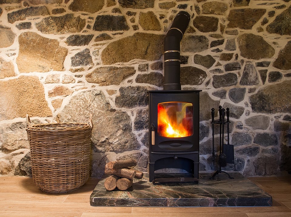 Adobe Stock image of a wood heating stove next to a pile of logs.