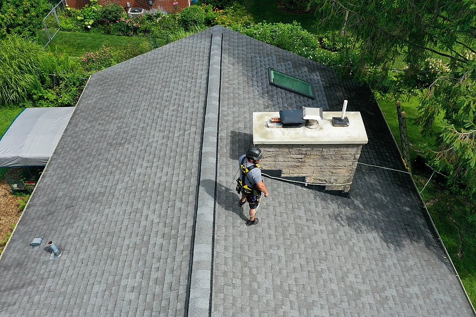 Original image of a chimney technician in a harness checking a chimney on a roof.
