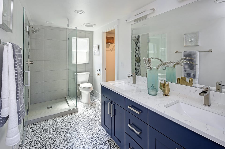 A bathroom with a clear shower, toilet, and blue cabinets under the sink.