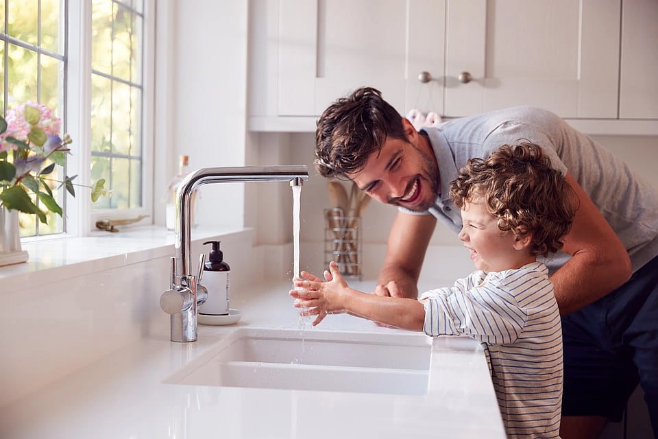 A father and son washing their hands together and laughing.