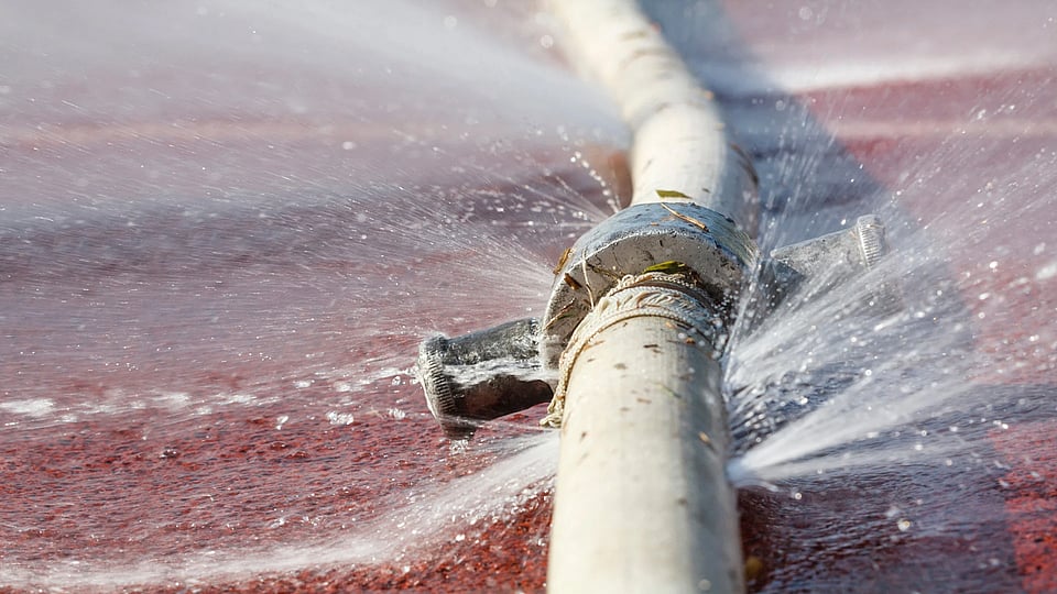 A water pipe with small holes that are leaking and spraying water.