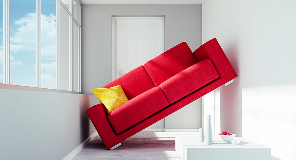 A red couch with a yellow pillow sitting crookedly and half on a wall in a small room.