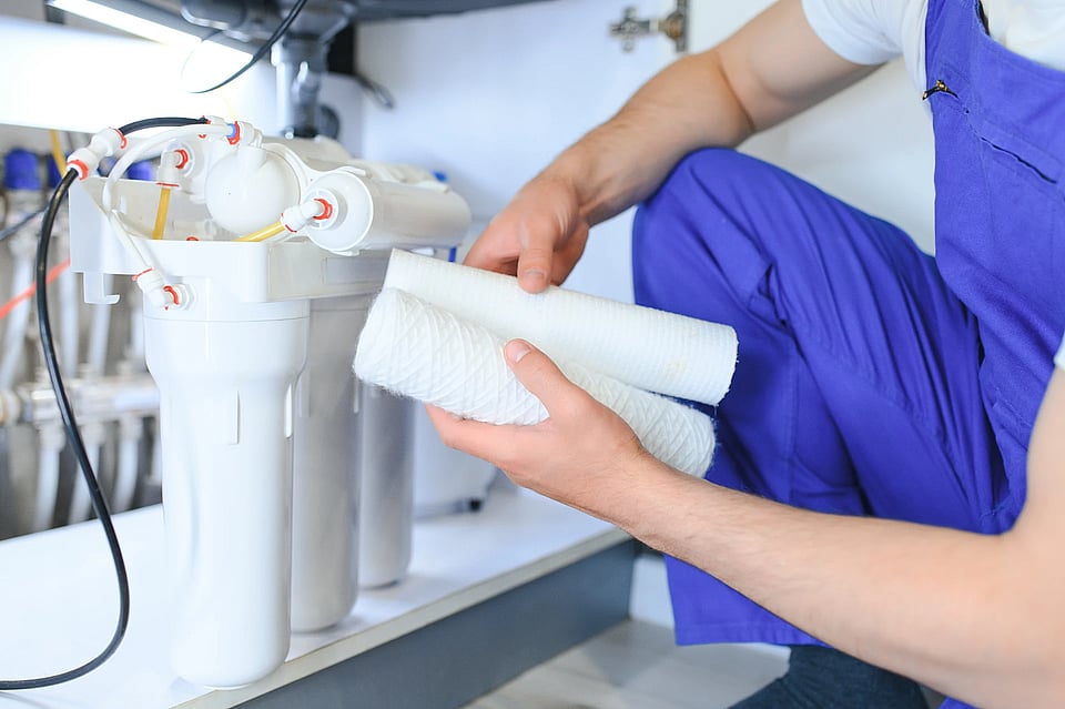 A service technician replacing filters on a reverse osmosis system.