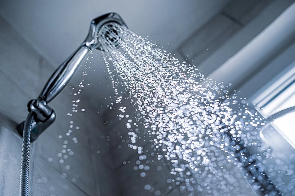 A silver shower header with water coming down at the camera.