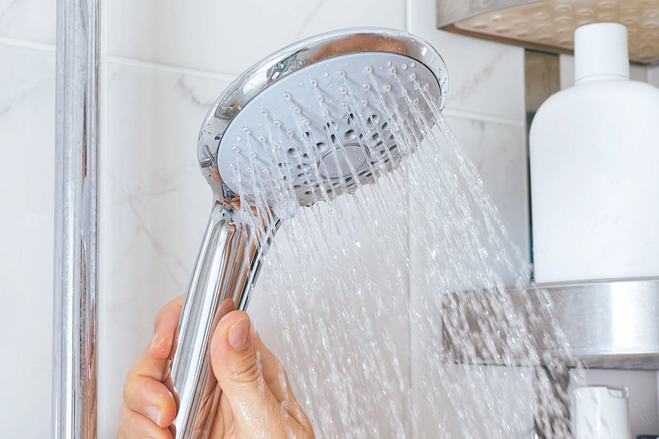 A shower head being held by someone as water is pouring out.