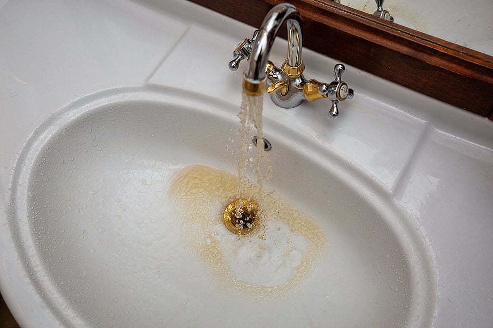 A white sink with silver faucet that’s pouring out red/rusty water.