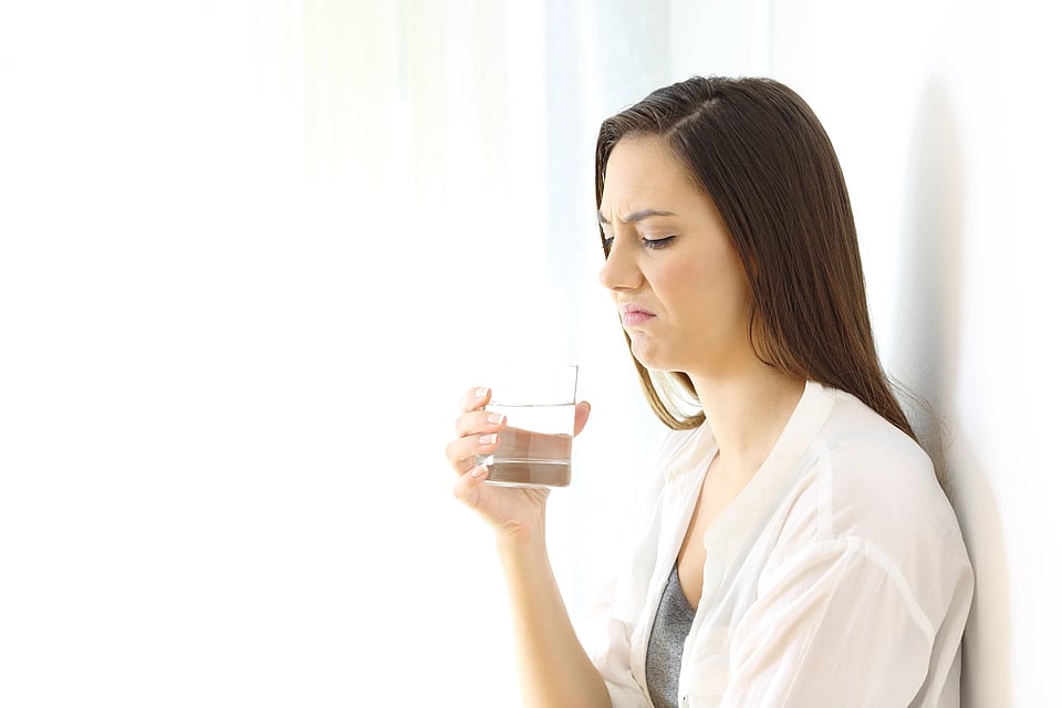A woman smelling a glass of water that doesn’t smell good.