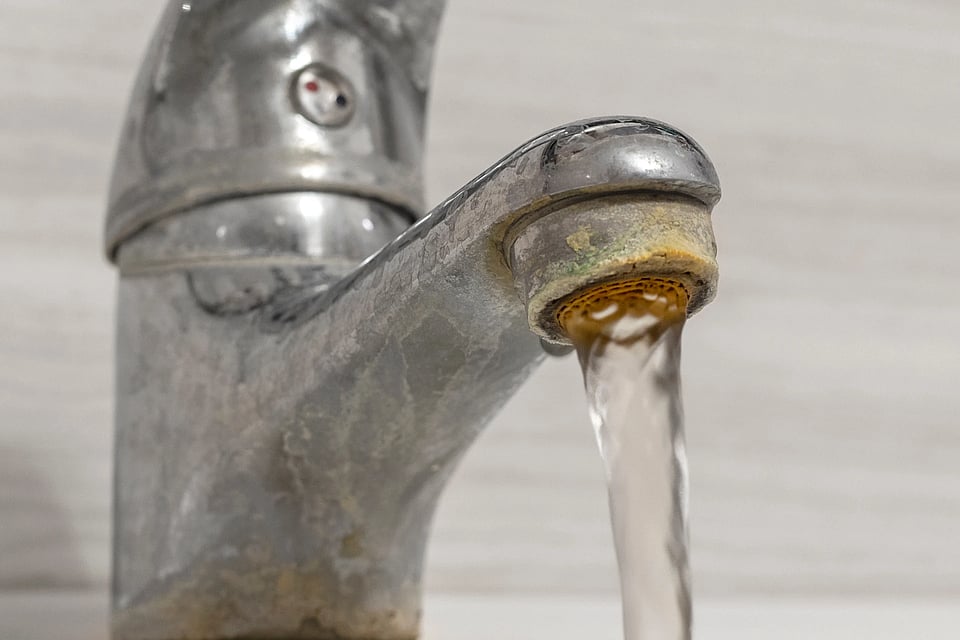 Scaled buildup on a faucet that has water coming out of it.