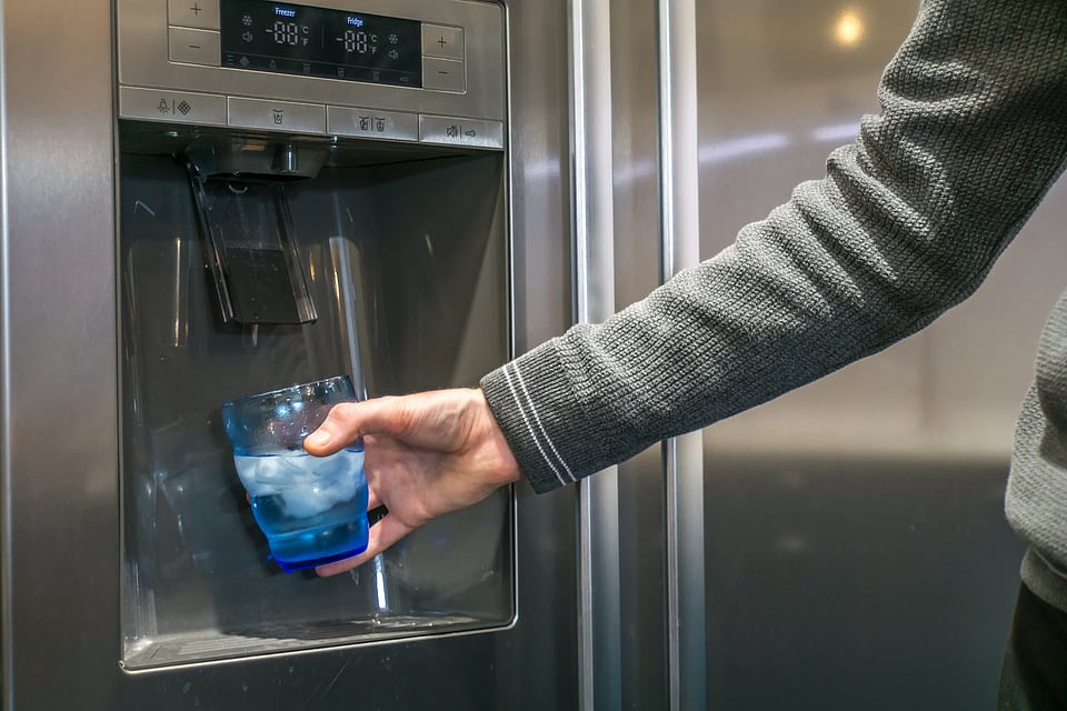 Someone using a blue glass to get water from a fridge filter.