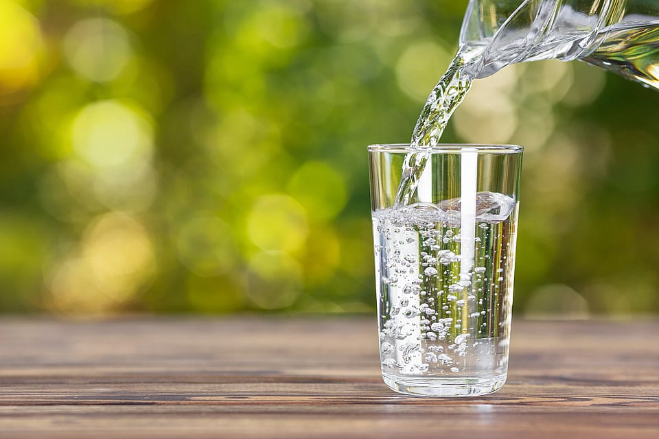Someone filling a glass of water from a pitcher outside.
