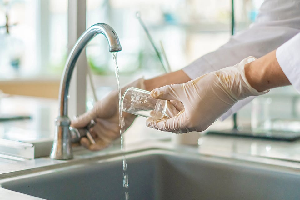Someone with gloves collecting a water sample from a faucet.