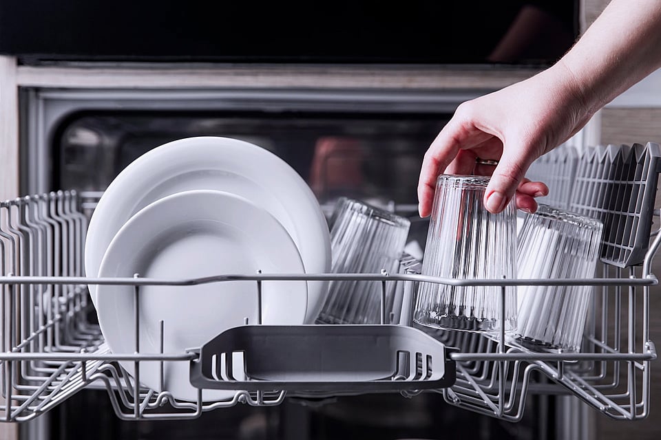 Someone remove clean, clear glasses from a dishwasher rack.