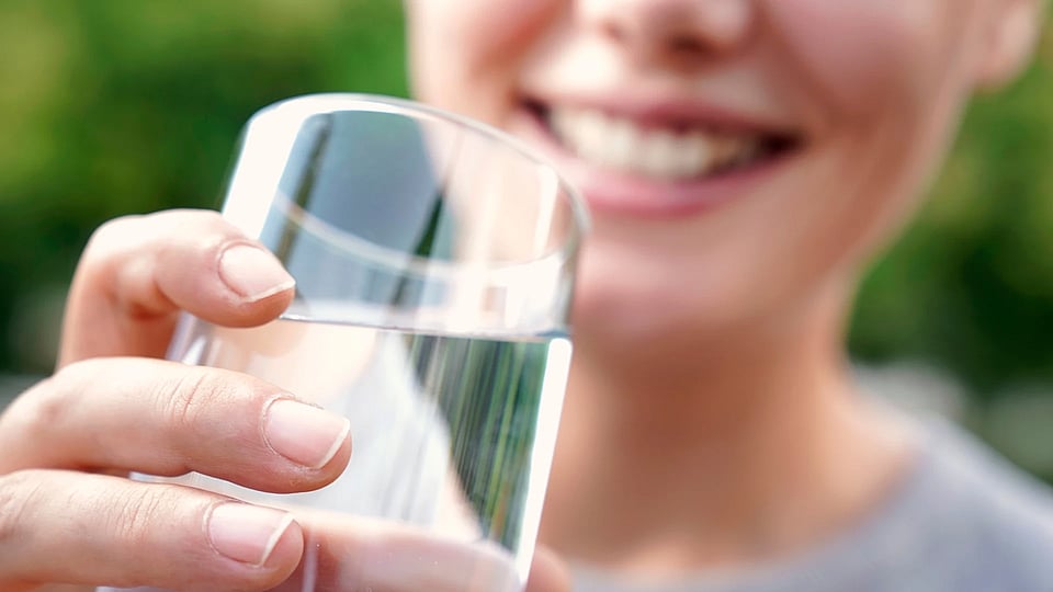 Someone holding a glass of water up to their mouth and smiling.