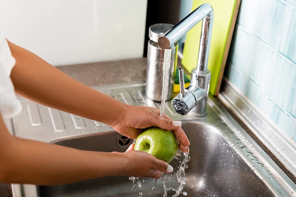 Someone washing a green apple in their sink.