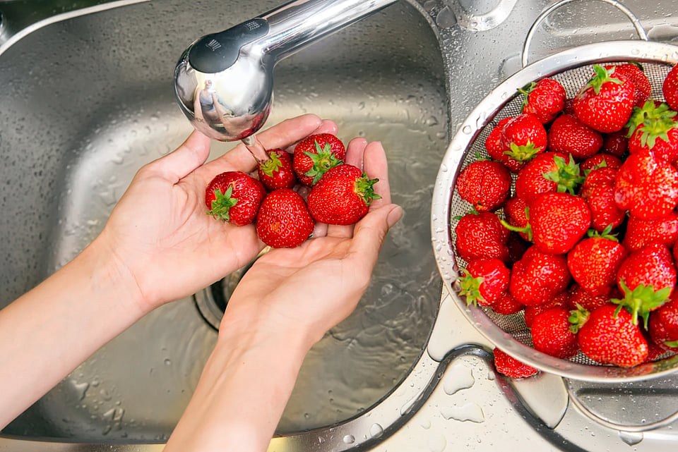 Someone washing strawberries in a sink.