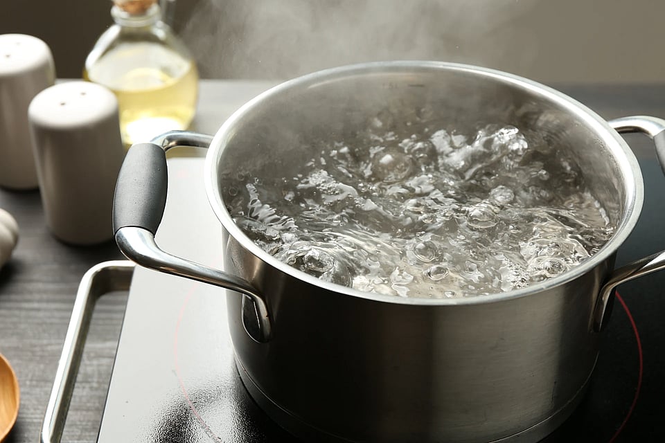 A pot of boiling water with spices and oil in the background.