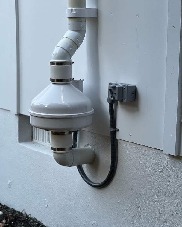 White radon mitigation fan and PVC piping installed on a residential exterior wall