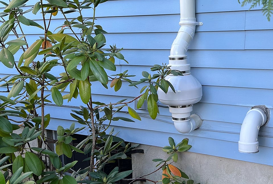 A white mitigation system on a house with blue siding.