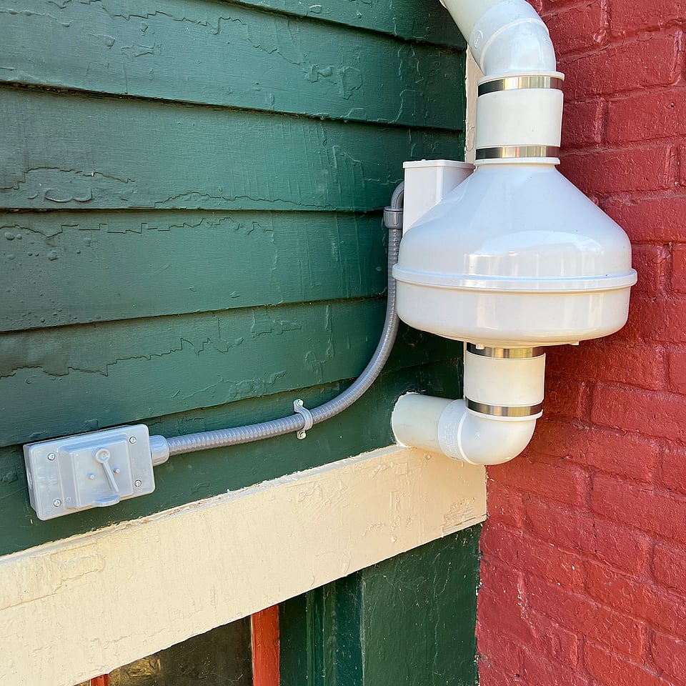 A radon mitigation system coming out of a hole in the exterior of a home.