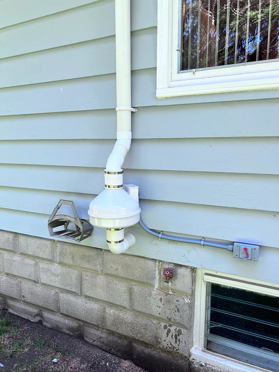 A white radon mitigation on a house with blue siding.