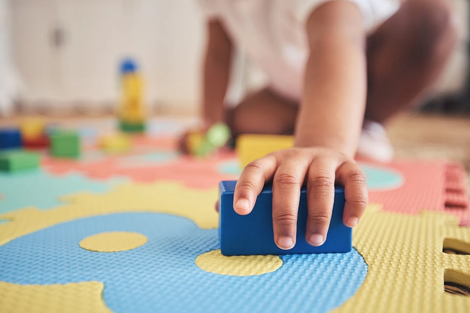 A small child reaching for a block in a daycare center.