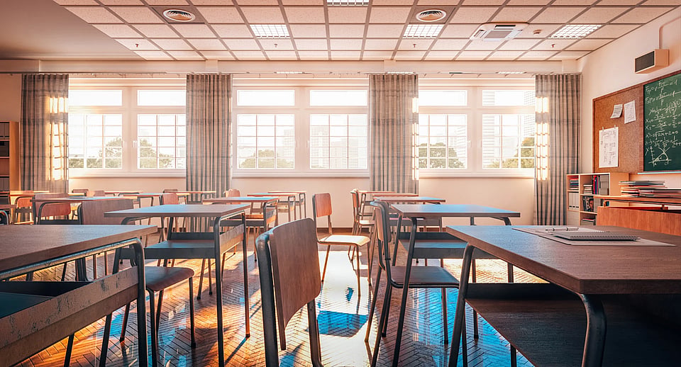 An empty classroom with desks and windows in the background.