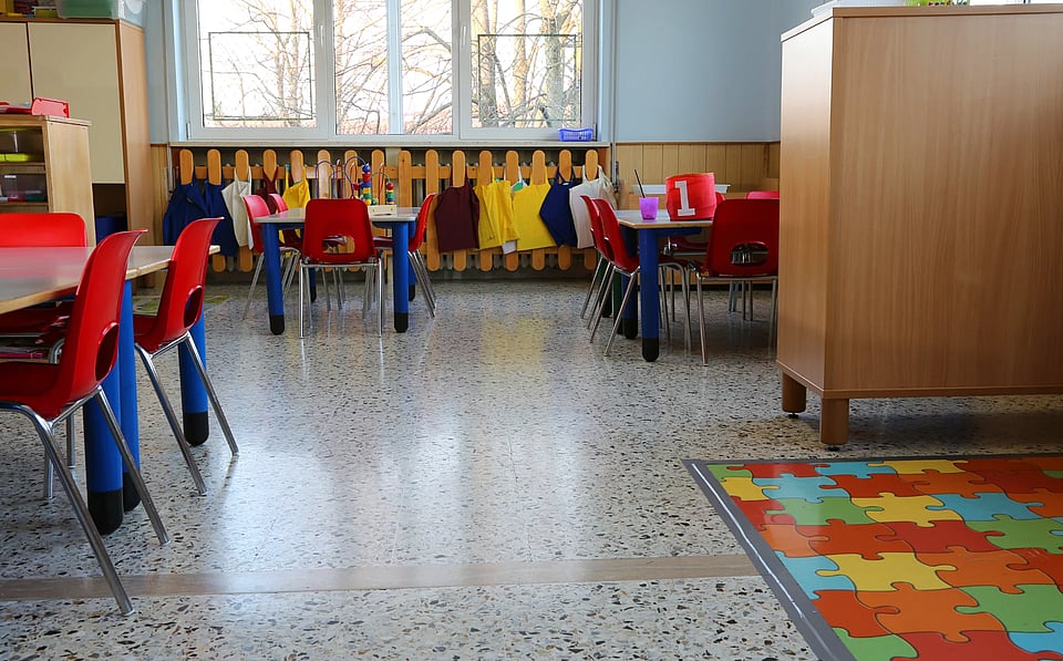 An empty daycare room with tables and small red chairs.