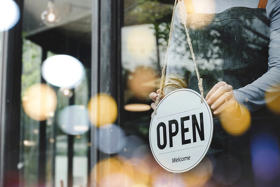 Someone turning a sign to open in the window of a business.