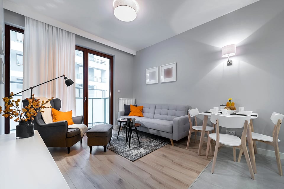 The interior of an apartment with a couch, table, chairs, and balcony view.