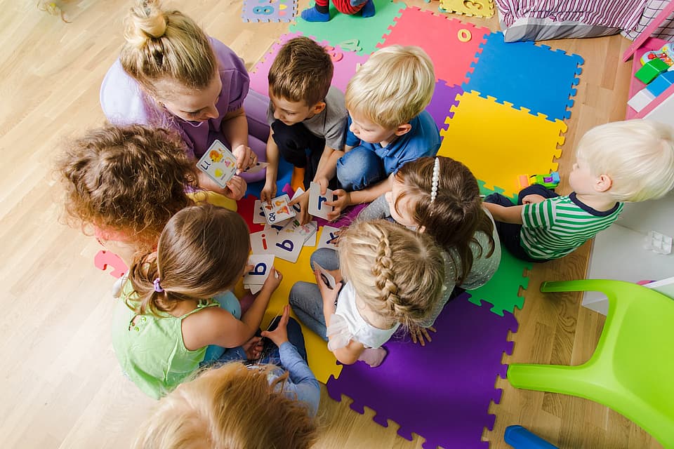 Kids sitting in a circle on a soft map with a daycare team learning about something.