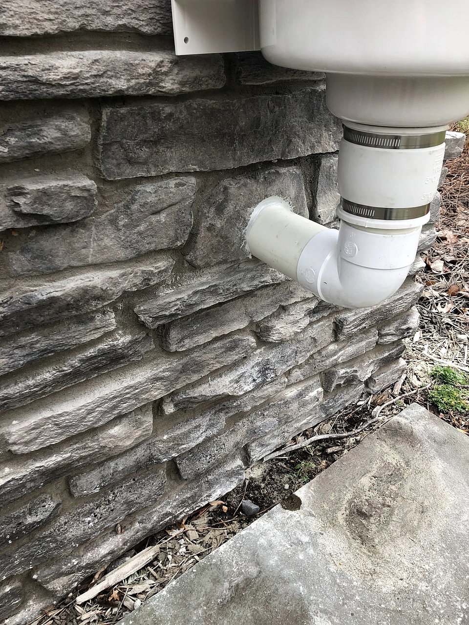 A close up shot of where a radon mitigation system goes into a brick house.