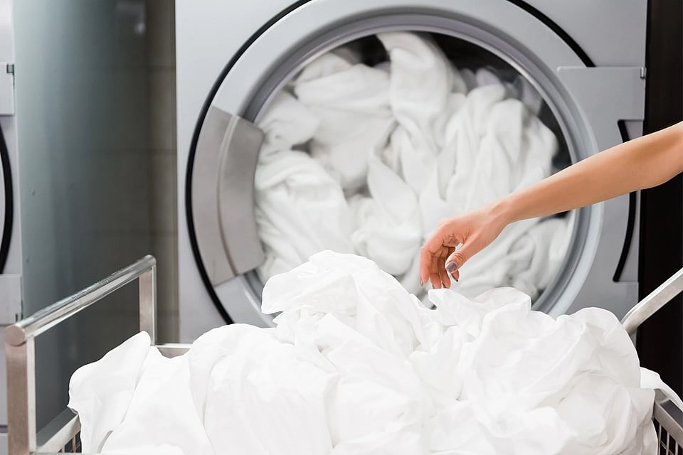 Adobe Stock image of a laundry machine in a hotel with sheets.