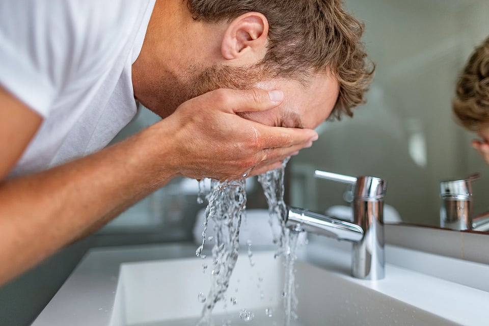 Adobe Stock image of a man splashing water on his face from the faucet.