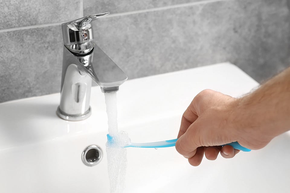 Adobe Stock image of a person running a toothbrush under running water from a sink.