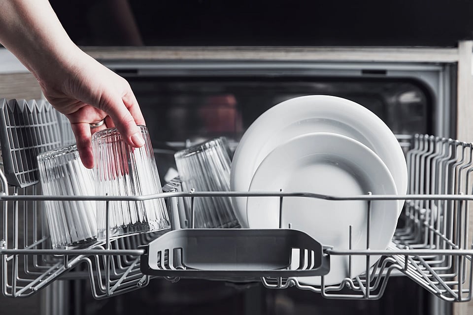 Adobe Stock image of a person unloading clean dishes from a dishwasher.