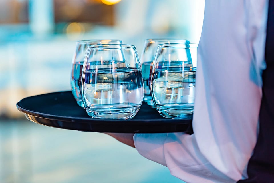 Adobe Stock image of a waiter carrying a tray of glasses.