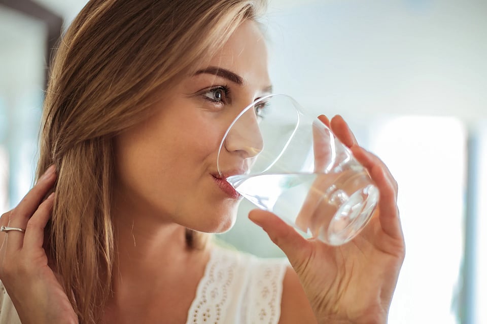 Adobe Stock image of a woman drinking clear water from a glass.