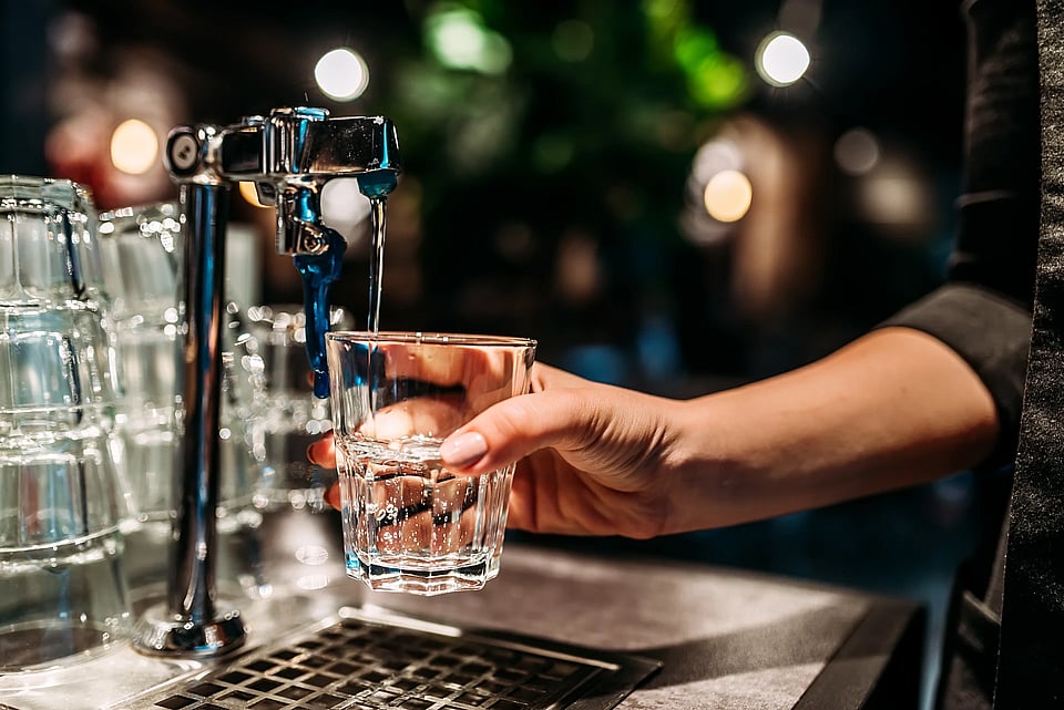 Adobe Stock image of water staff filling a glass of water from a spout.