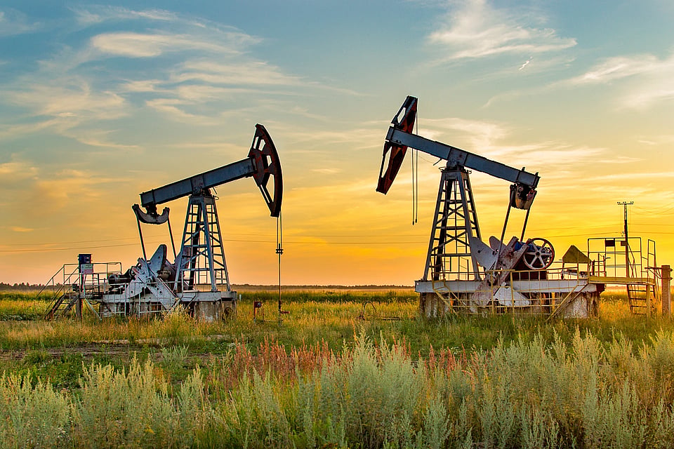 Adobe Stock image of well drilling rigs against a sunset.