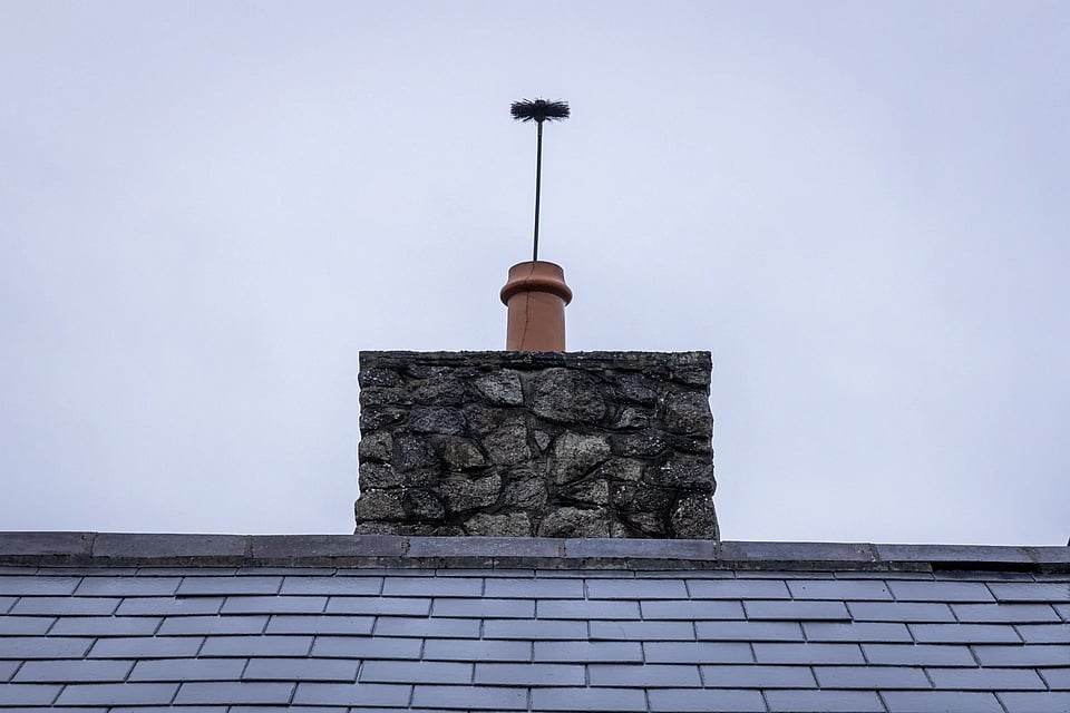 Adobe Stock image of a chimney sweep brush coming out the top of a chimney flue.