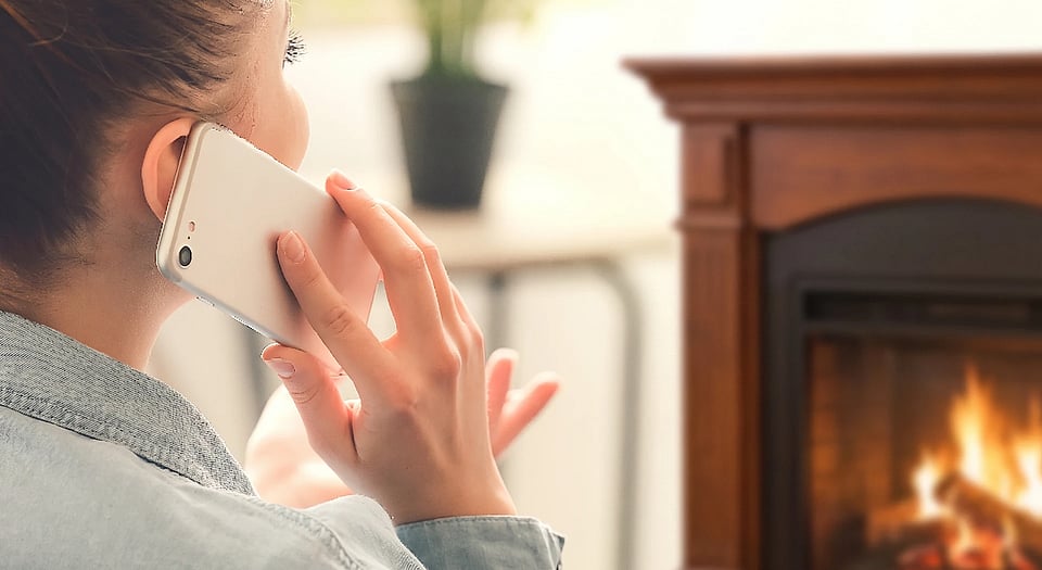 Stock image of a woman making a phone call near a fireplace.