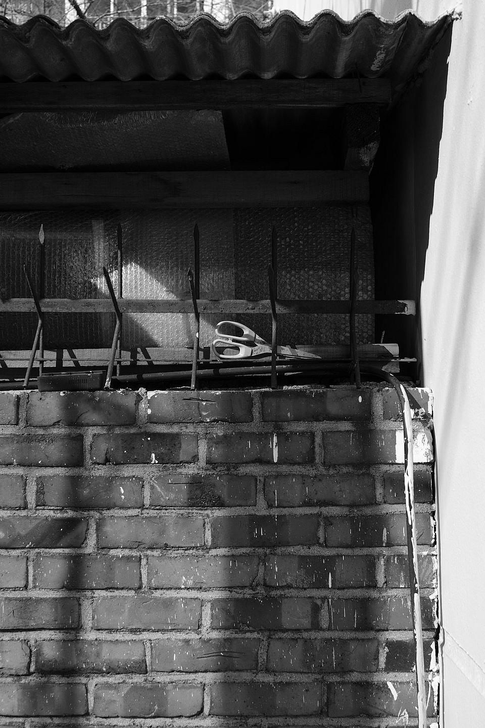 Black-and-white photo of a weathered brick wall with metal rails and a corrugated roof overhang above it