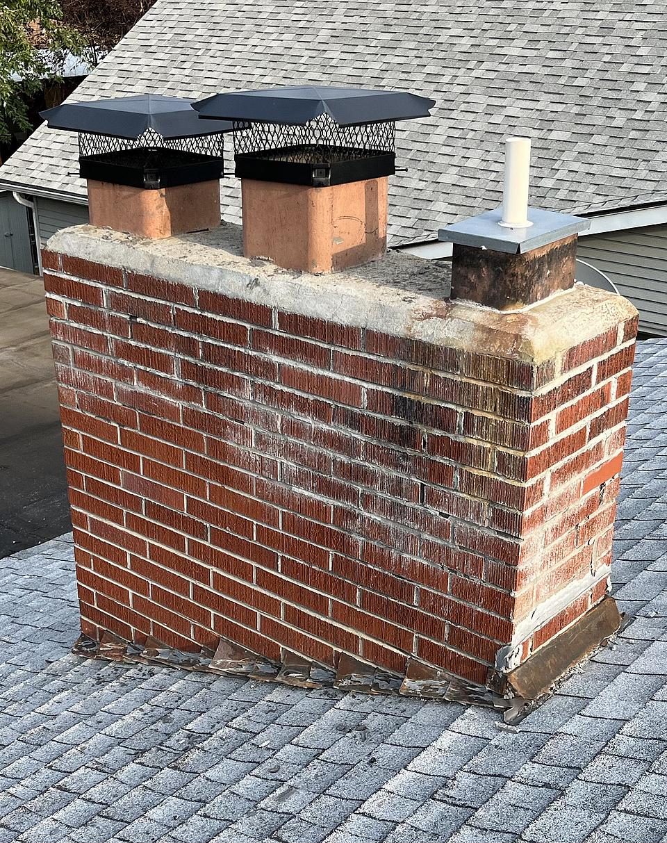 Red brick chimney with two black metal chimney caps on a grey shingle roof